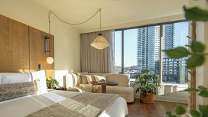 A modern hotel room with a large bed, a sofa, a small table, and a view of tall buildings. - 1 Hotel Seattle (Seattle)