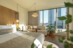 A modern hotel room with a large bed, a sofa, a small table, and a view of tall buildings. - 1 Hotel Seattle (Seattle)