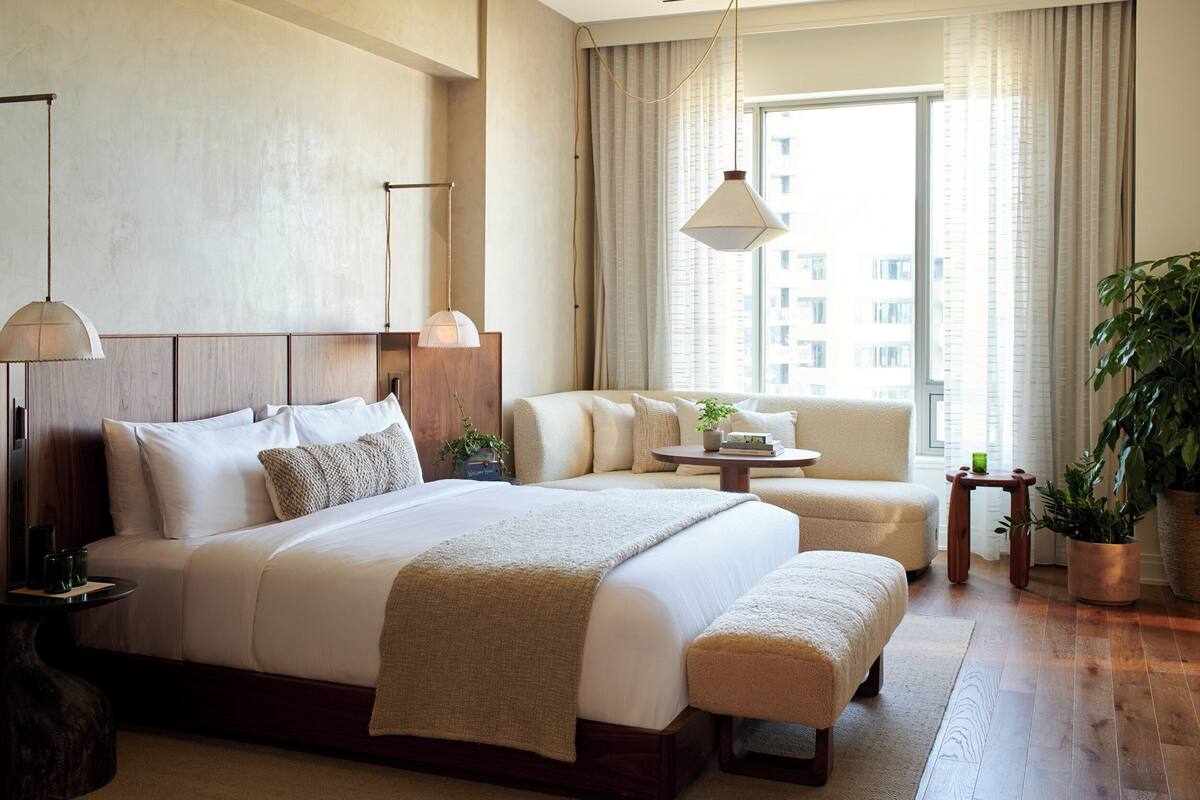 A hotel room with a large bed, a sofa, a small table, and a potted plant.