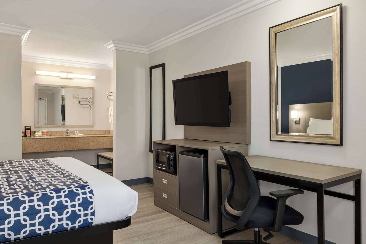 A hotel room with a bed, a desk, a TV, a microwave, and a large mirror.