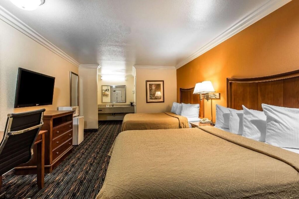 A hotel room with two beds, a desk, a television, and a bathroom.
