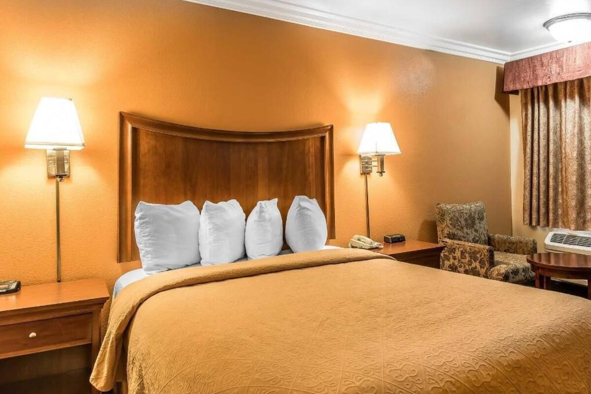 A hotel room with a large bed, two bedside lamps, a chair, a desk, and a telephone.