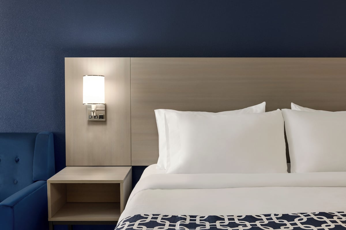 A hotel room with a bed, a bedside table, a lamp, and a blue chair.