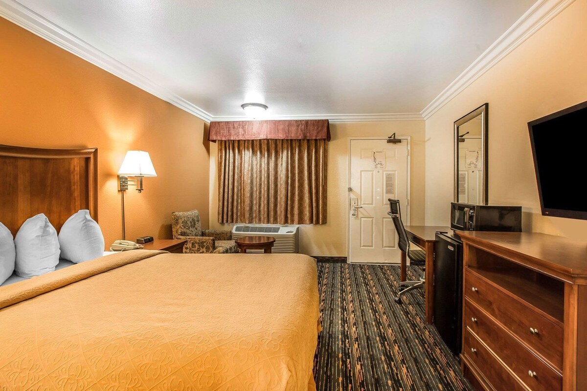 A hotel room with a bed, a desk, a chair, a dresser, a television, and a door.