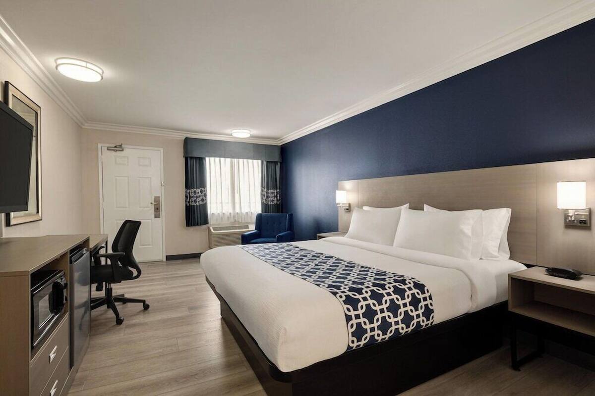 A hotel room with a large bed, a desk, a chair, a television, and a door.