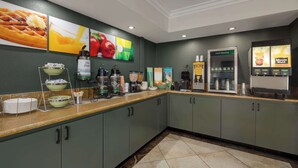 A breakfast bar with various food items and beverages, including a coffee machine, a fruit display, and a juice dispenser. - Quality Inn Lake Elsinore I-15 (Lake Elsinore)