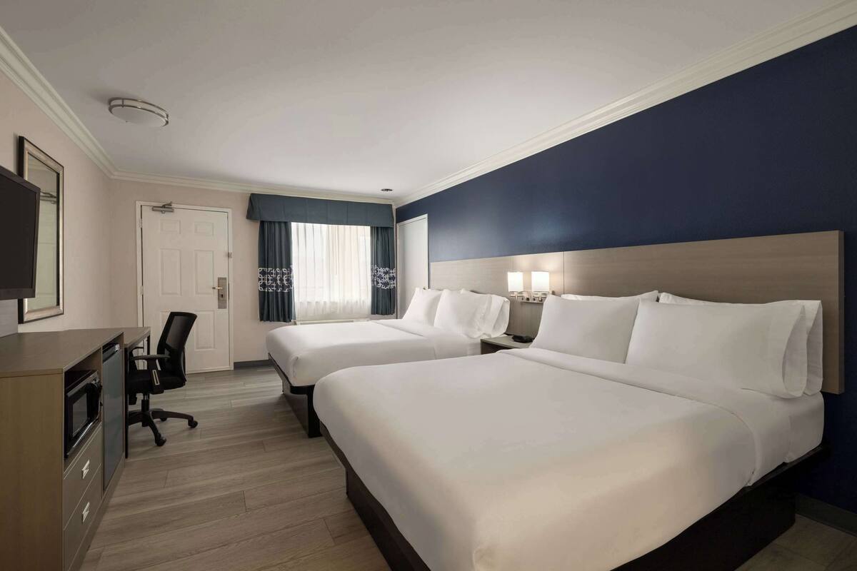A hotel room with two beds, a desk with a chair, a television, and a window with curtains.