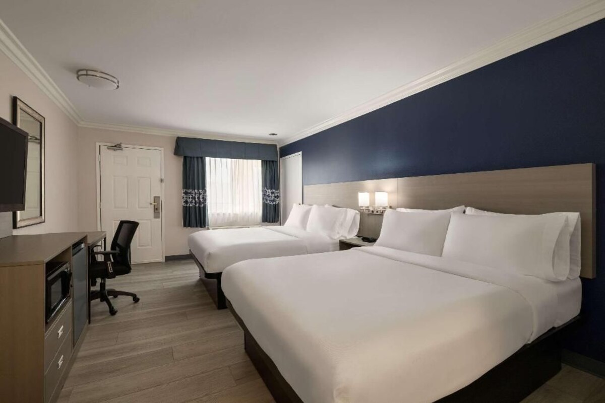 A hotel room with two beds, a desk, a chair, a television, and a window with curtains.