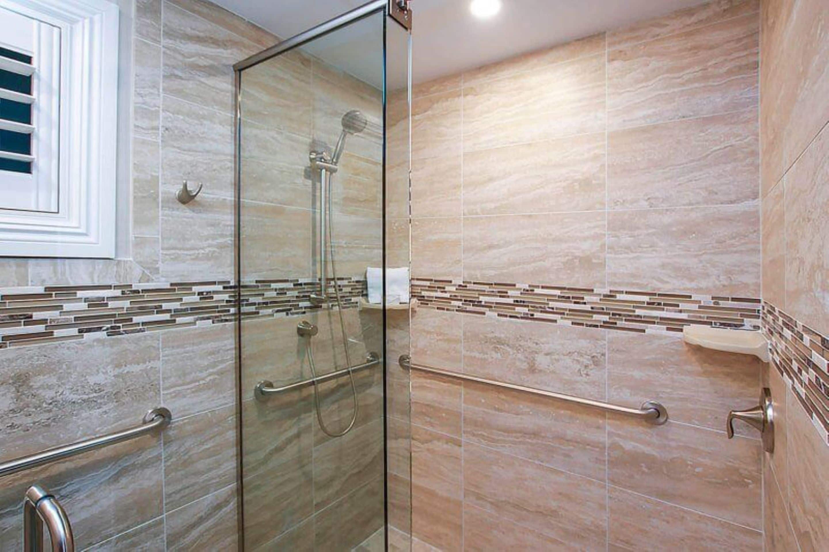 Une salle de bain moderne avec une douche à parois de verre, des murs carrelés et une barre d’appui.