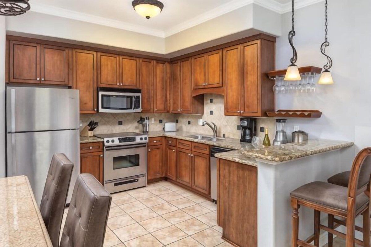 A kitchen with wooden cabinets, stainless steel appliances, a granite countertop, and a dining area with chairs.