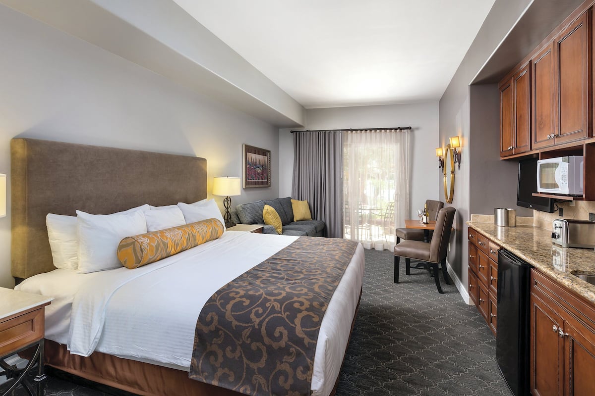 A hotel room with a large bed, a desk, a chair, a television, and a kitchenette.