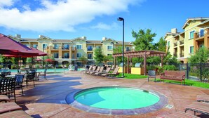A pool area with lounge chairs and umbrellas, surrounded by multi-story buildings with balconies. - Vino Bello Resort (Napa)
