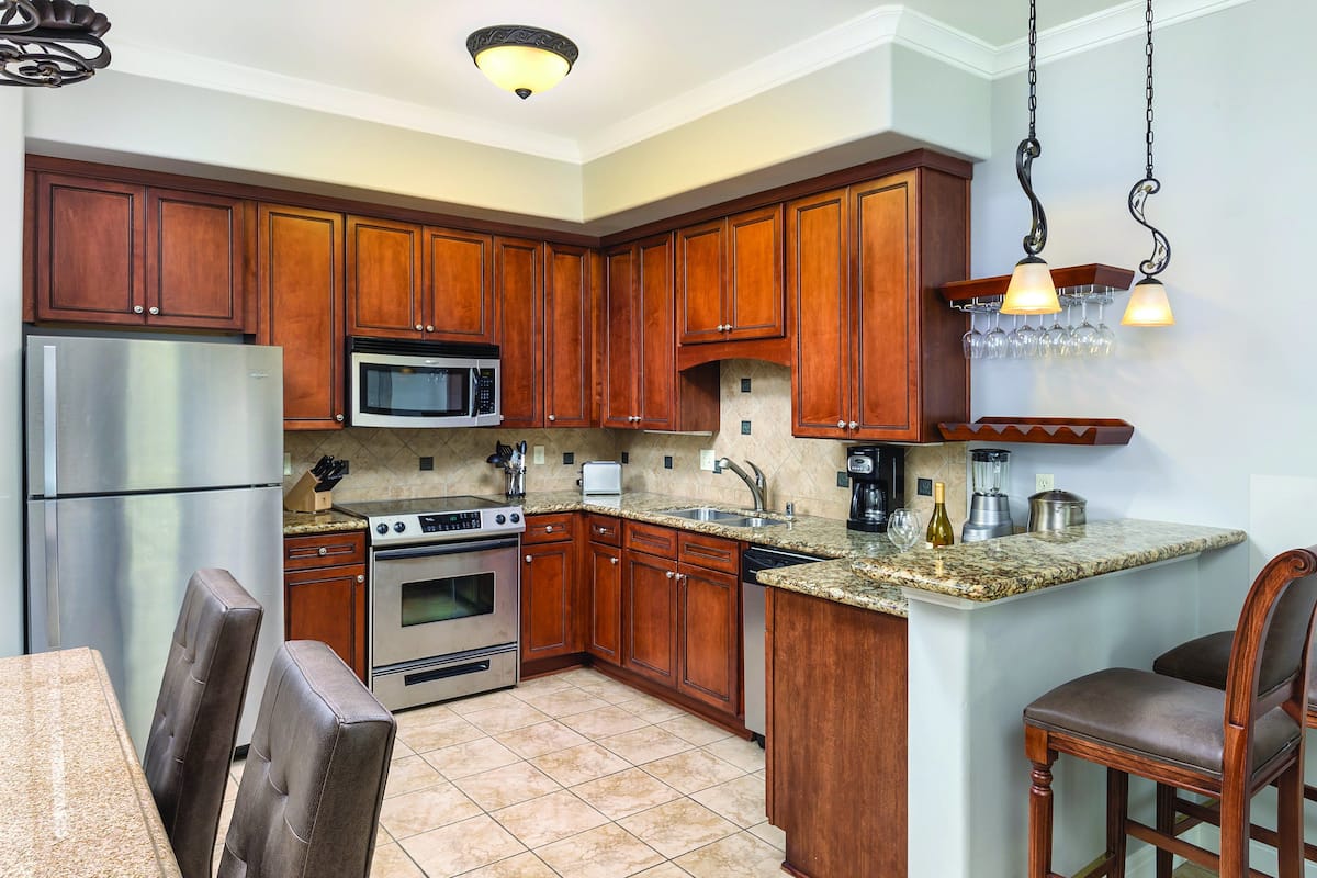 A kitchen with wooden cabinets, stainless steel appliances, granite countertops, and a dining area with leather chairs.