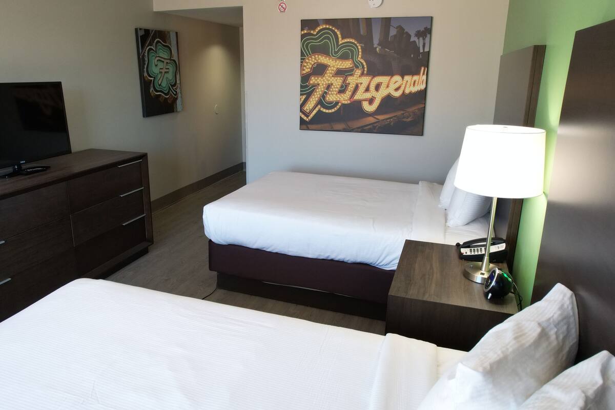 Une chambre d’hôtel avec deux lits, une télévision, une commode et une lampe.