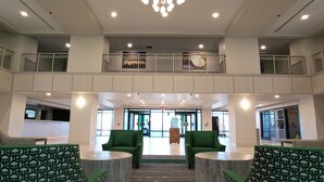 A hotel lobby with a double-height ceiling, green seating, and a reception desk.