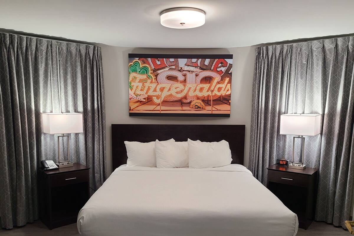 Une chambre d’hôtel avec un grand lit, deux tables de chevet avec des lampes, une horloge et un tableau accroché au mur.