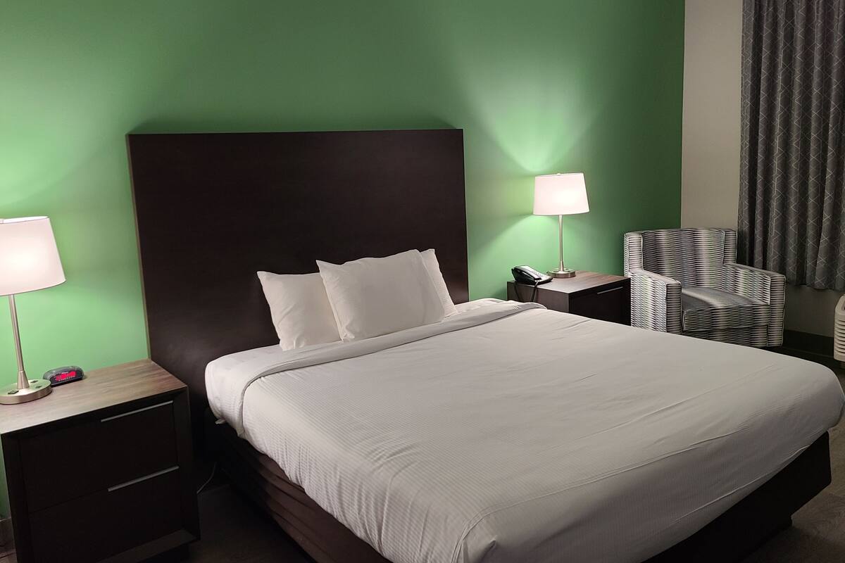 Une chambre d’hôtel avec un grand lit, deux tables de chevet, une lampe, une chaise et un mur vert.
