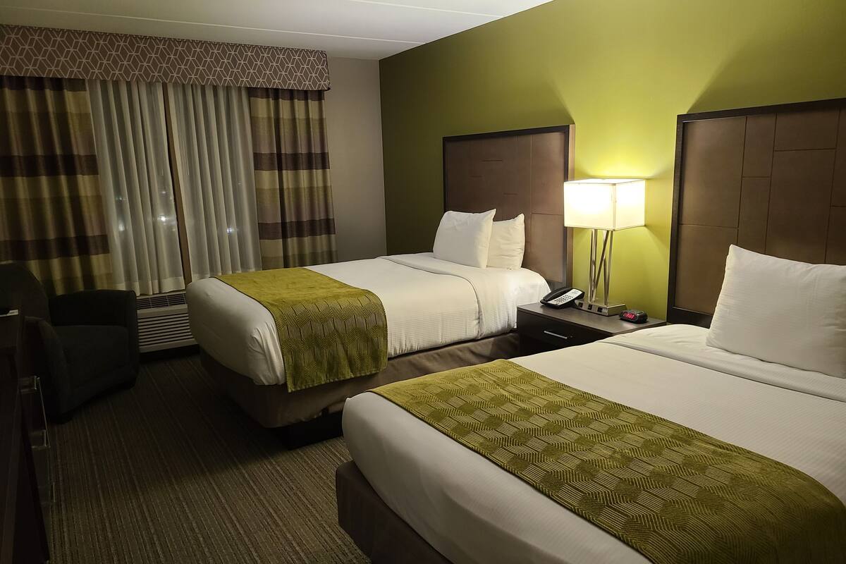 Une chambre d’hôtel avec deux lits, un bureau, une chaise, une lampe et une fenêtre avec des rideaux.