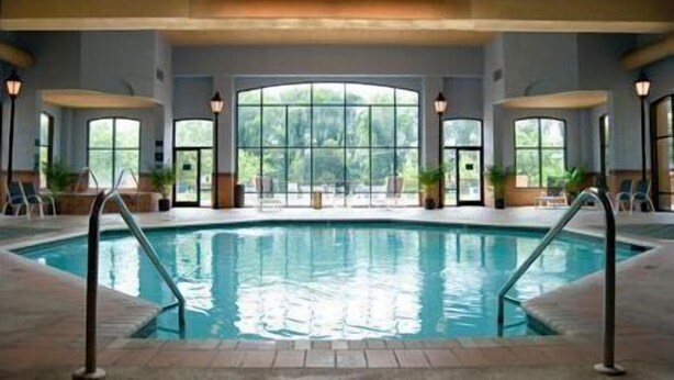 An indoor swimming pool with clear glass walls, lounge chairs, and potted plants.