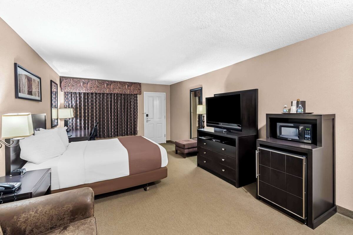 A hotel room with a bed, a TV, a microwave, a dresser, and a desk with a lamp.