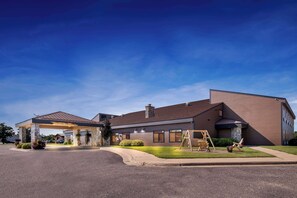 A modern hotel with a covered entrance, a stone facade, and a well-maintained lawn.