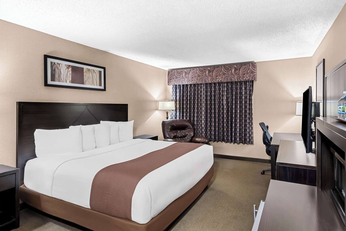 A hotel room with a large bed, a desk, a chair, a television, and a window with curtains.
