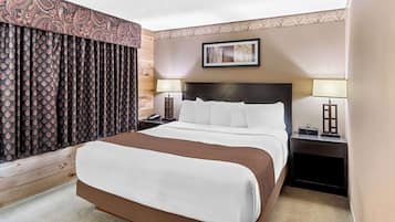 Une chambre d’hôtel avec un grand lit, deux tables de chevet avec des lampes, un tableau encadré au mur et un rideau à motifs.