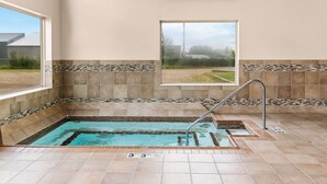 A rectangular indoor pool with a metal ladder, surrounded by beige walls with decorative tile borders. - Heartland Inn & Suites, SureStay Collection by Best Western (Park Rapids)