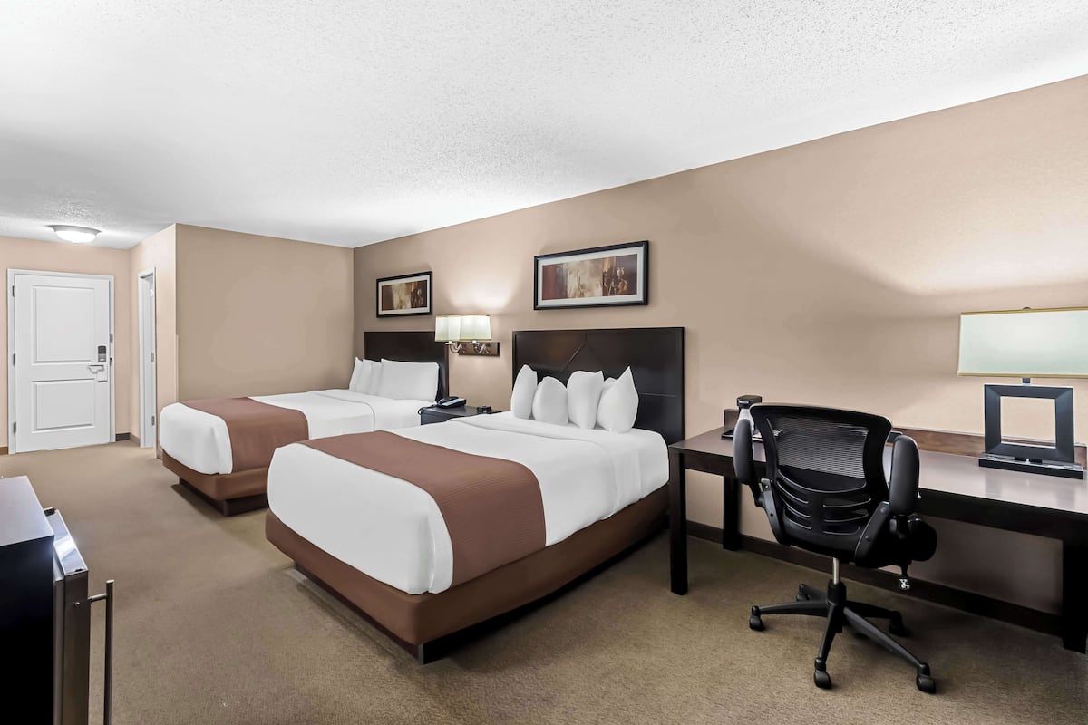 A hotel room with two beds, a desk, a chair, and a door.