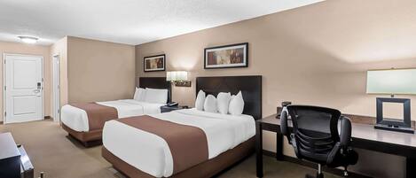 A hotel room with two beds, a desk, a chair, and a door.