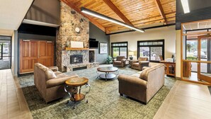 A spacious living area with leather sofas, a stone fireplace, and large windows. - Heartland Inn & Suites, SureStay Collection by Best Western (Park Rapids)
