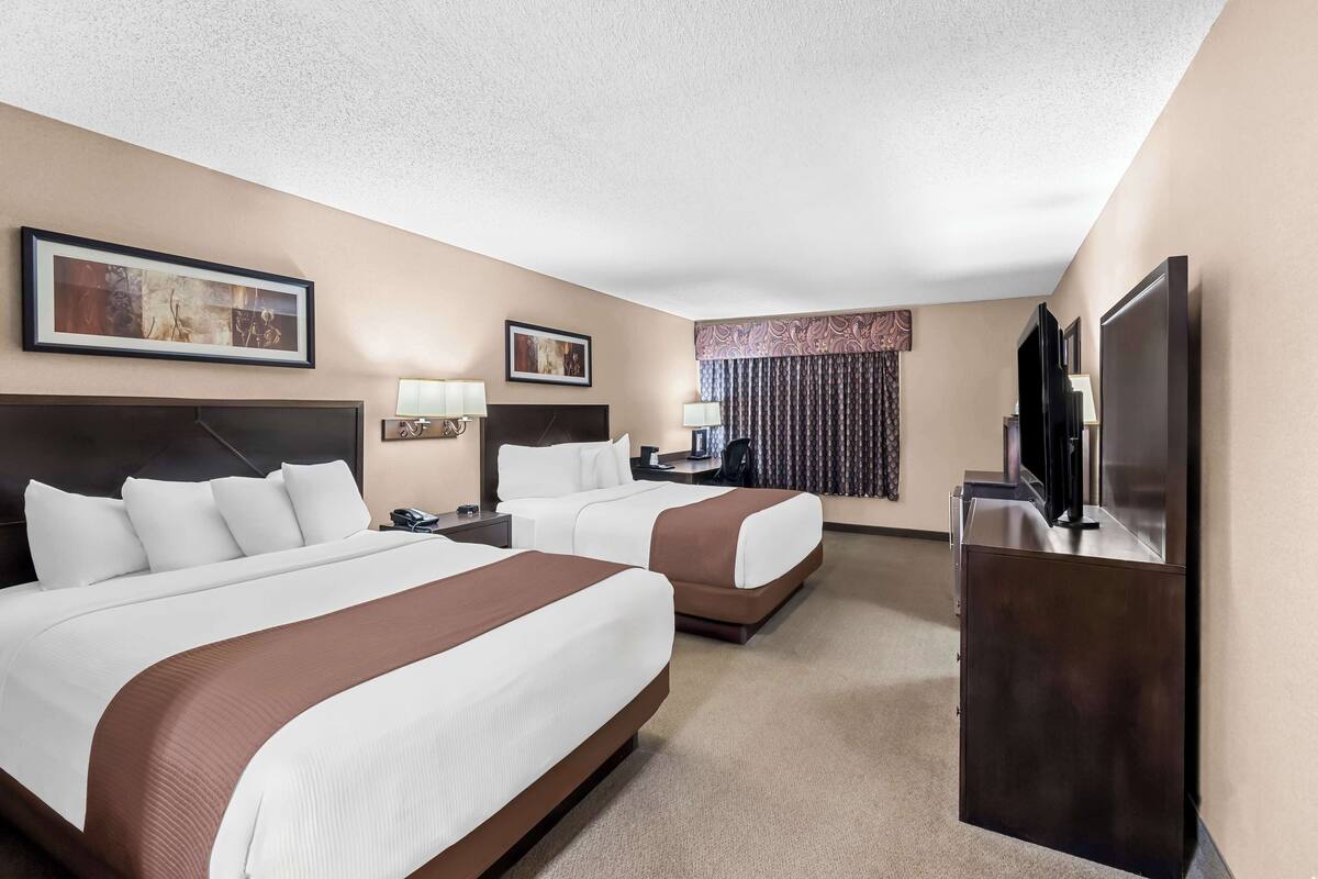 A hotel room with two beds, a desk, a TV, and a large window with curtains.