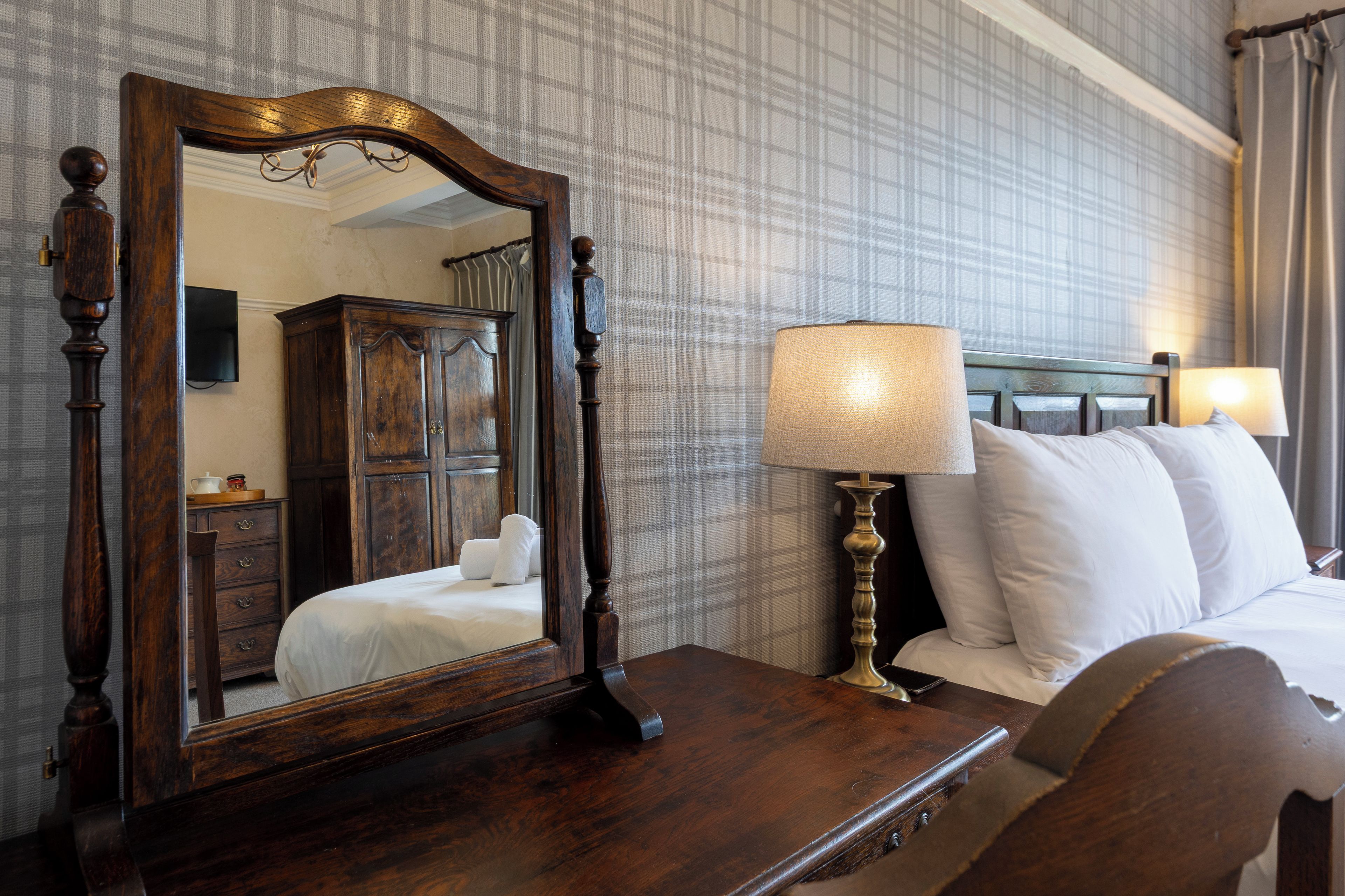Ein Hotelzimmer mit einem großen Spiegel, einer Holzkommode, einem Bett mit weißen Leinen und einem Nachttisch mit einer Lampe.