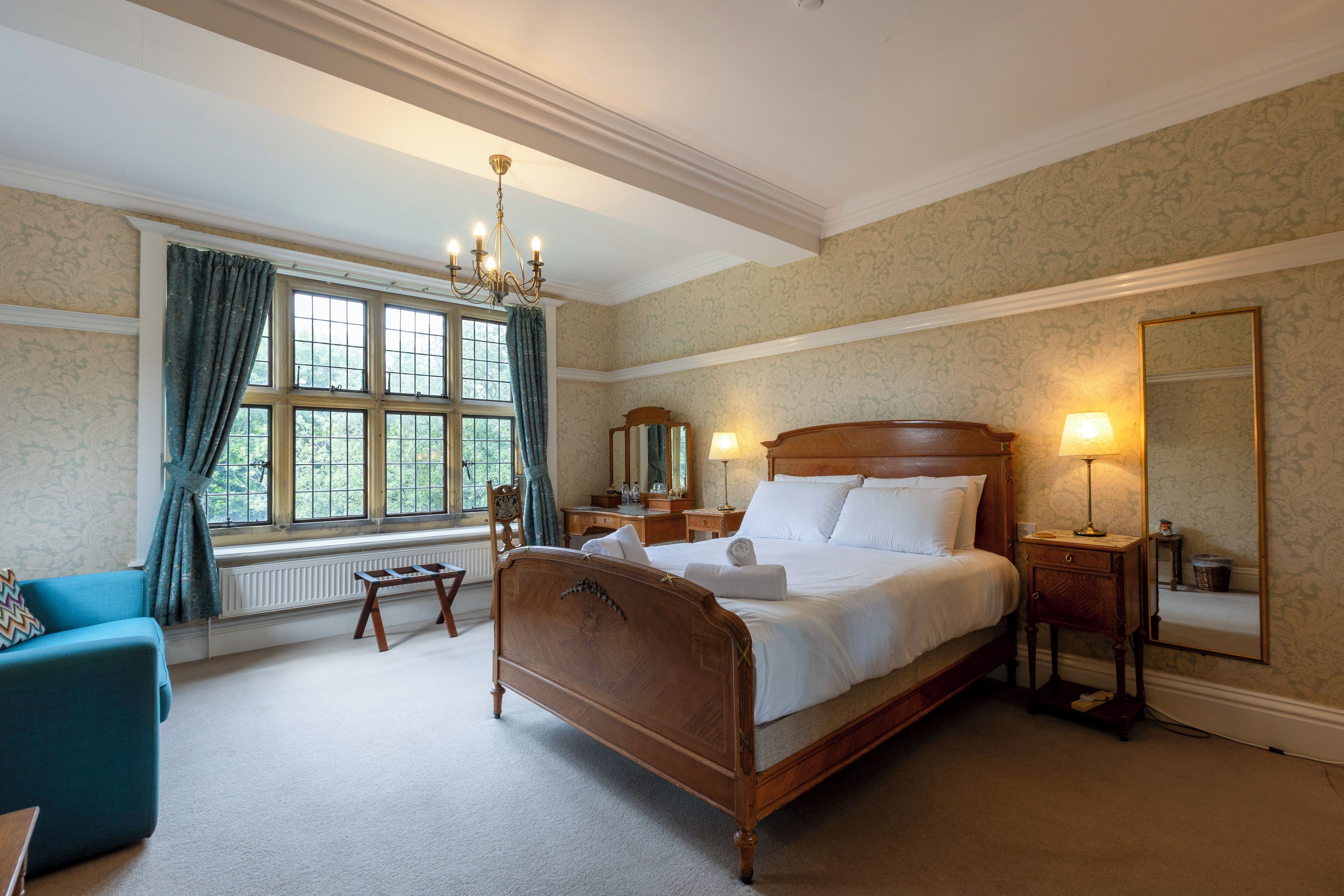 A well-lit bedroom with a large bed, a dresser, a chair, and a window with curtains.