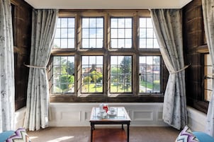 A room with a large window, a small table with a teapot and cups, and floral curtains.