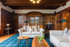Une pièce de style traditionnel avec un plafond en bois, une grande bibliothèque, deux canapés, une table basse et un tapis à motifs.