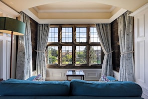 A room with a large bay window, a sofa, a table, and curtains. - Dunsley Hall Country House Hotel (Whitby)