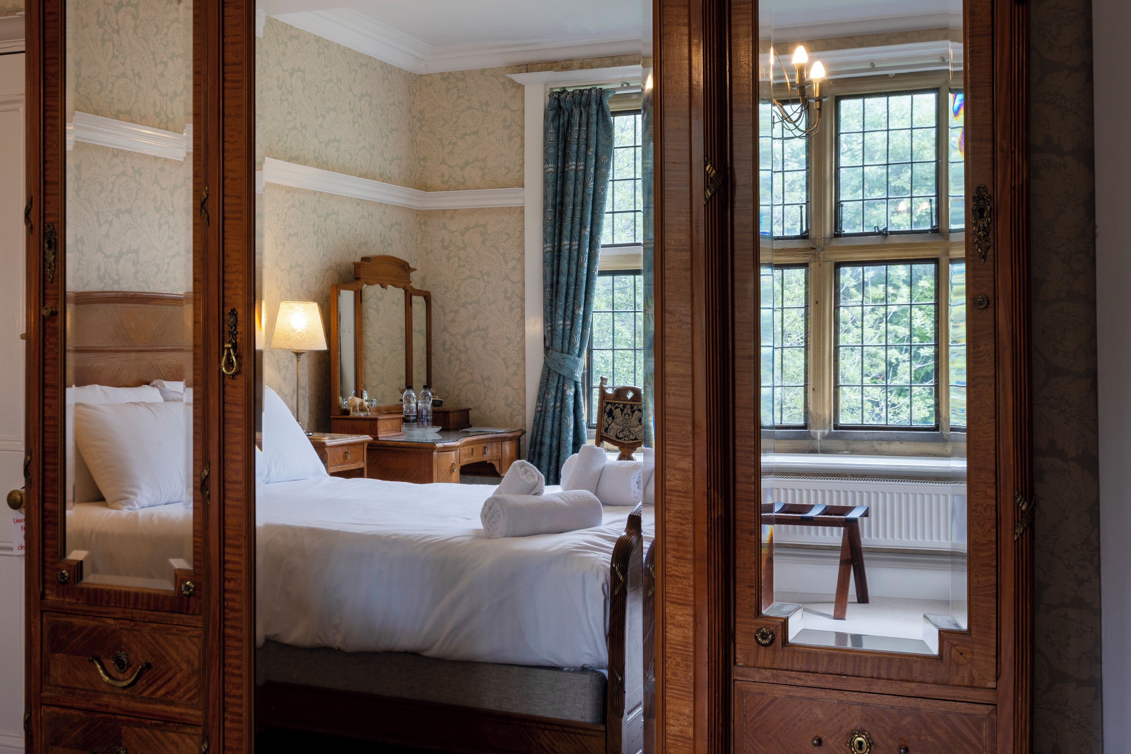 A hotel room with a large bed, a dresser, a mirror, a window with curtains, and a radiator.