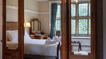 A hotel room with a large bed, a dresser, a mirror, a window with curtains, and a radiator.