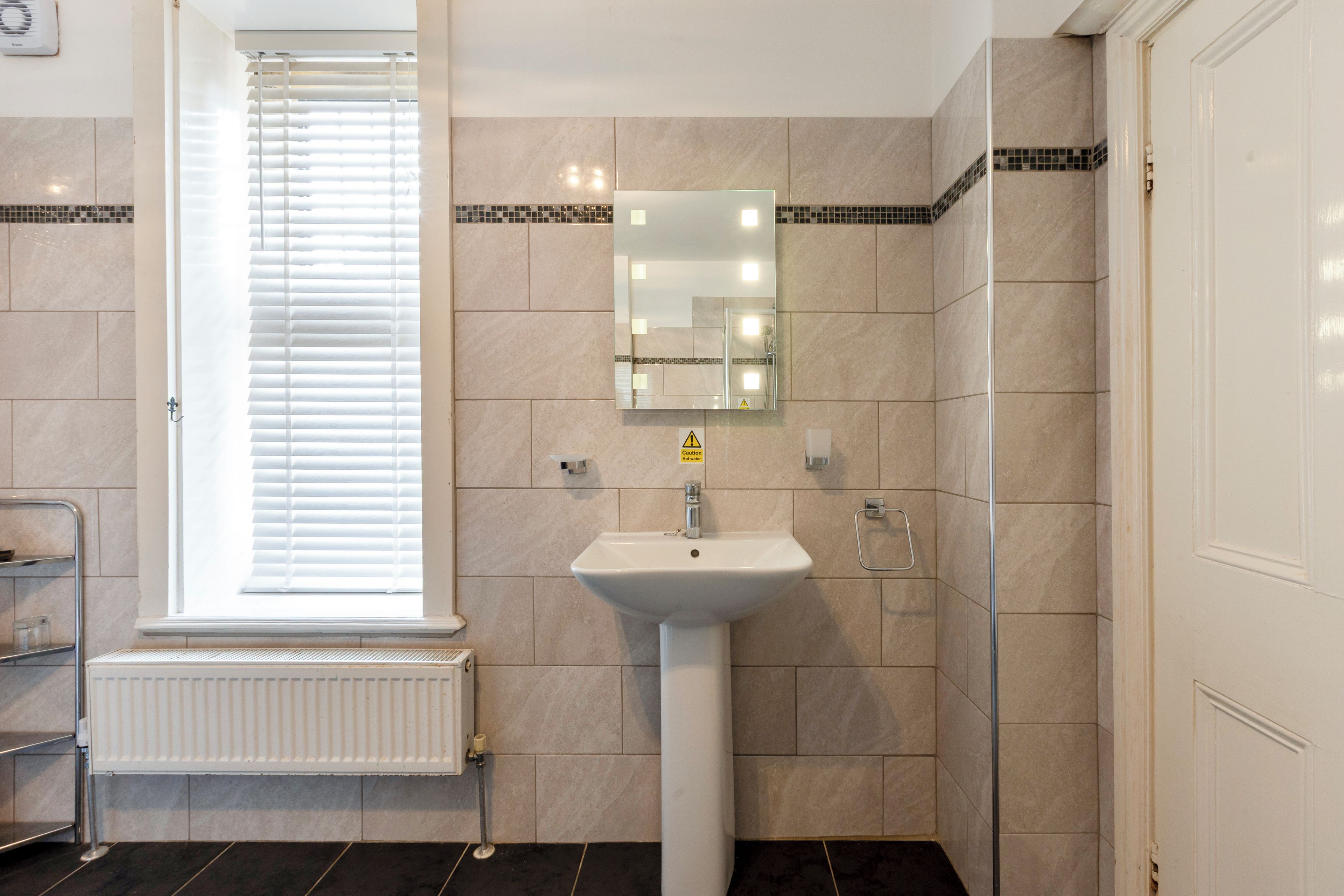 A bathroom with a white sink, a mirror, and a window with blinds.