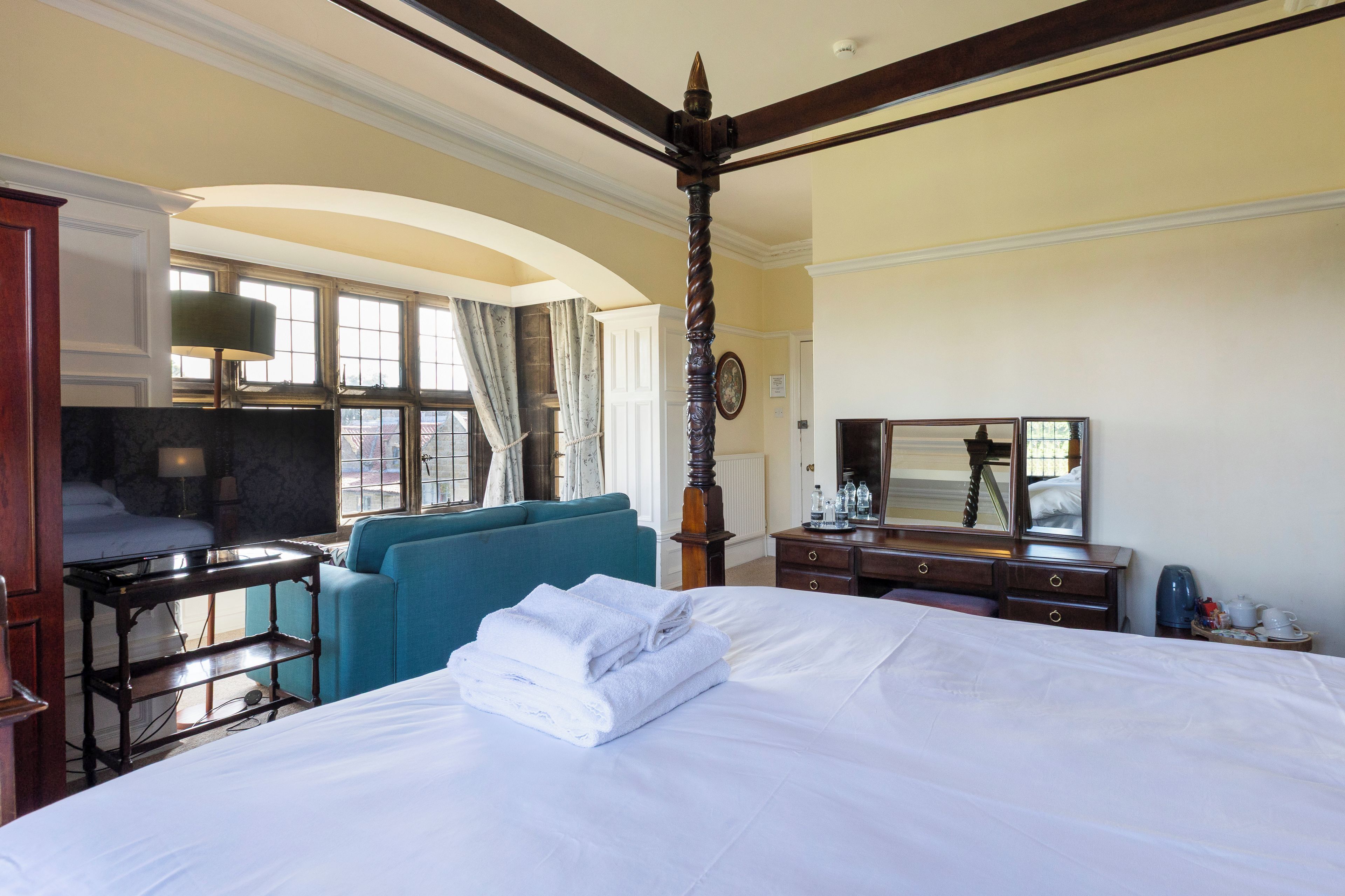 A hotel room with a large bed, a sitting area with a blue sofa, a desk with a lamp, and a dresser with a mirror.
