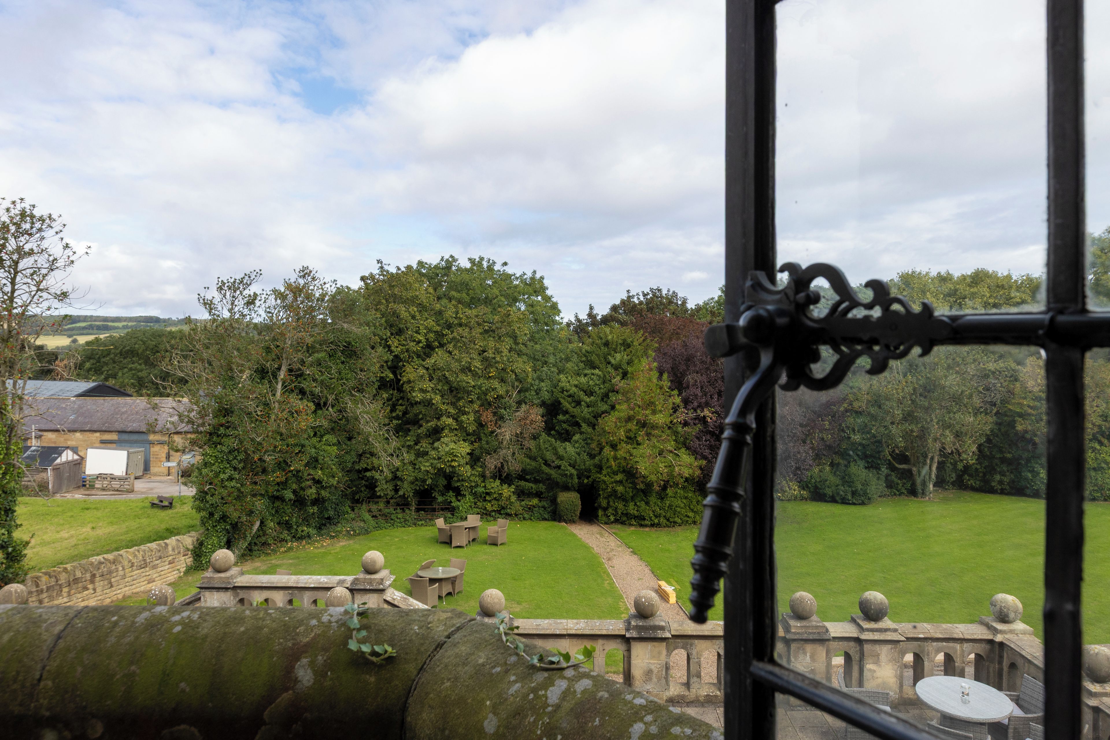 A view of a garden with a stone balustrade, a lawn, and a building in the background.