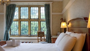 A hotel room with a large window, a bed with white linens, a wooden chair, and two bedside lamps. - Dunsley Hall Country House Hotel (Whitby)