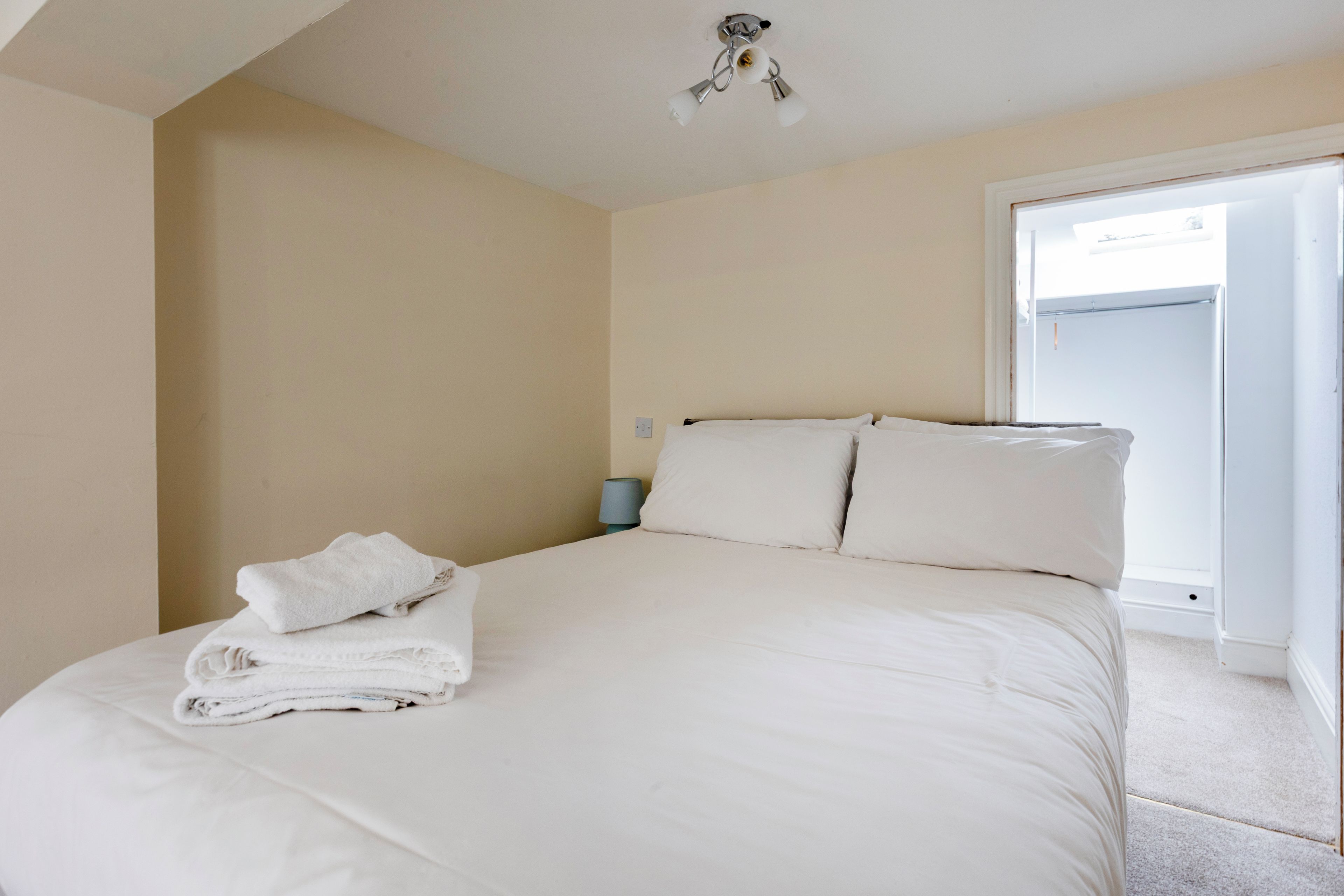 A bedroom with a bed, pillows, a folded towel, a nightstand, and a window.