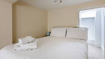 A bedroom with a bed, pillows, a folded towel, a nightstand, and a window.