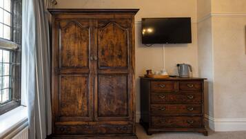 Una habitación con un armario de madera grande, un pequeño tocador con cajones, un televisor de pantalla plana en la pared y una ventana con cortinas.