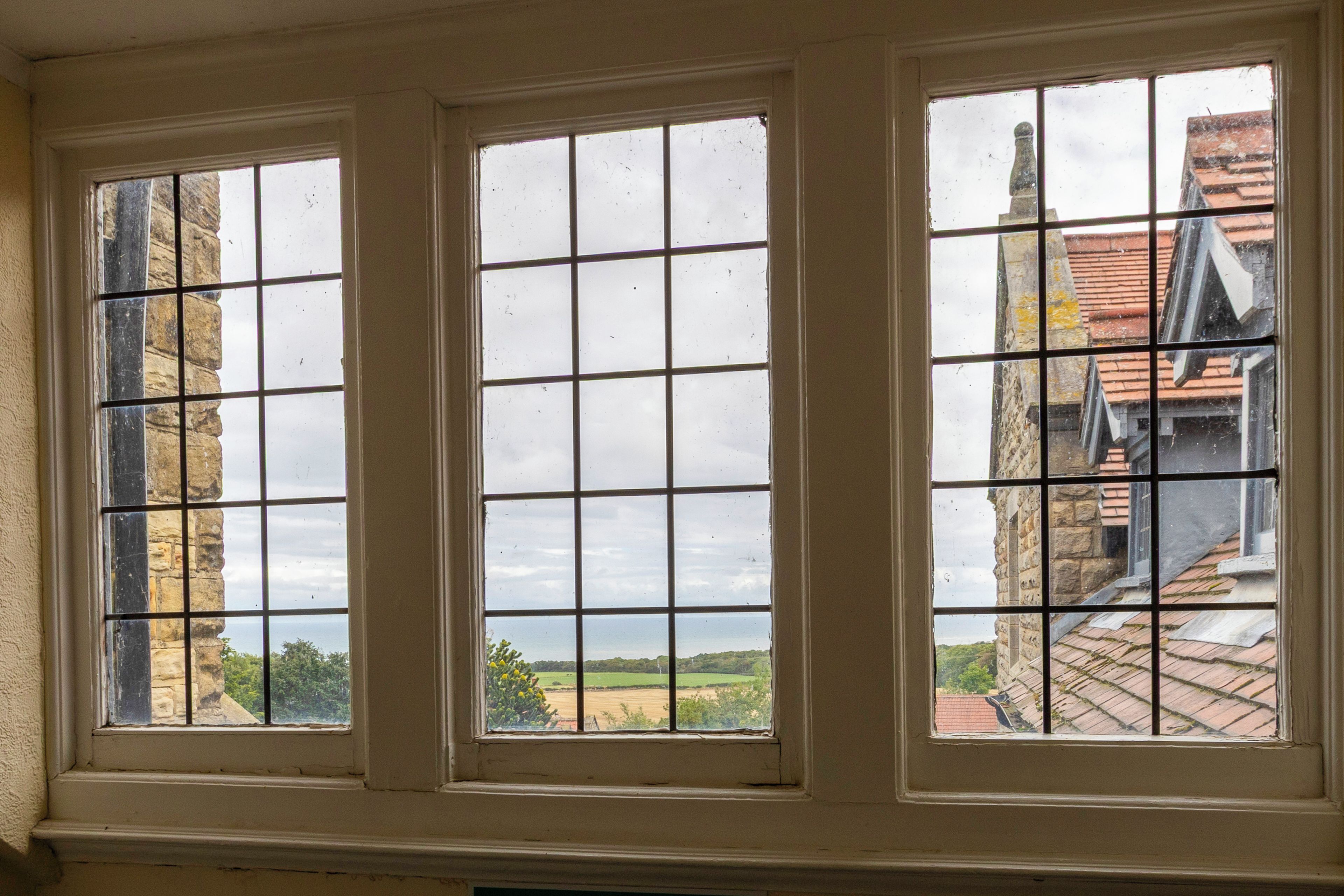 A window with a grid pattern, overlooking a rural landscape with fields and a distant building.