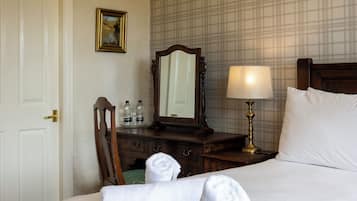 Een hotelkamer met een bed, nachtkastje, spiegel, lamp, dressoir en een deur.