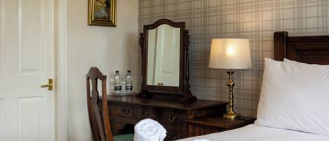A hotel room with a bed, a nightstand, a mirror, a lamp, a dresser, and a door.