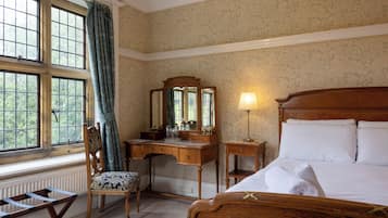 A hotel room with a wooden bed, a desk with a mirror, a chair, and a window with curtains.